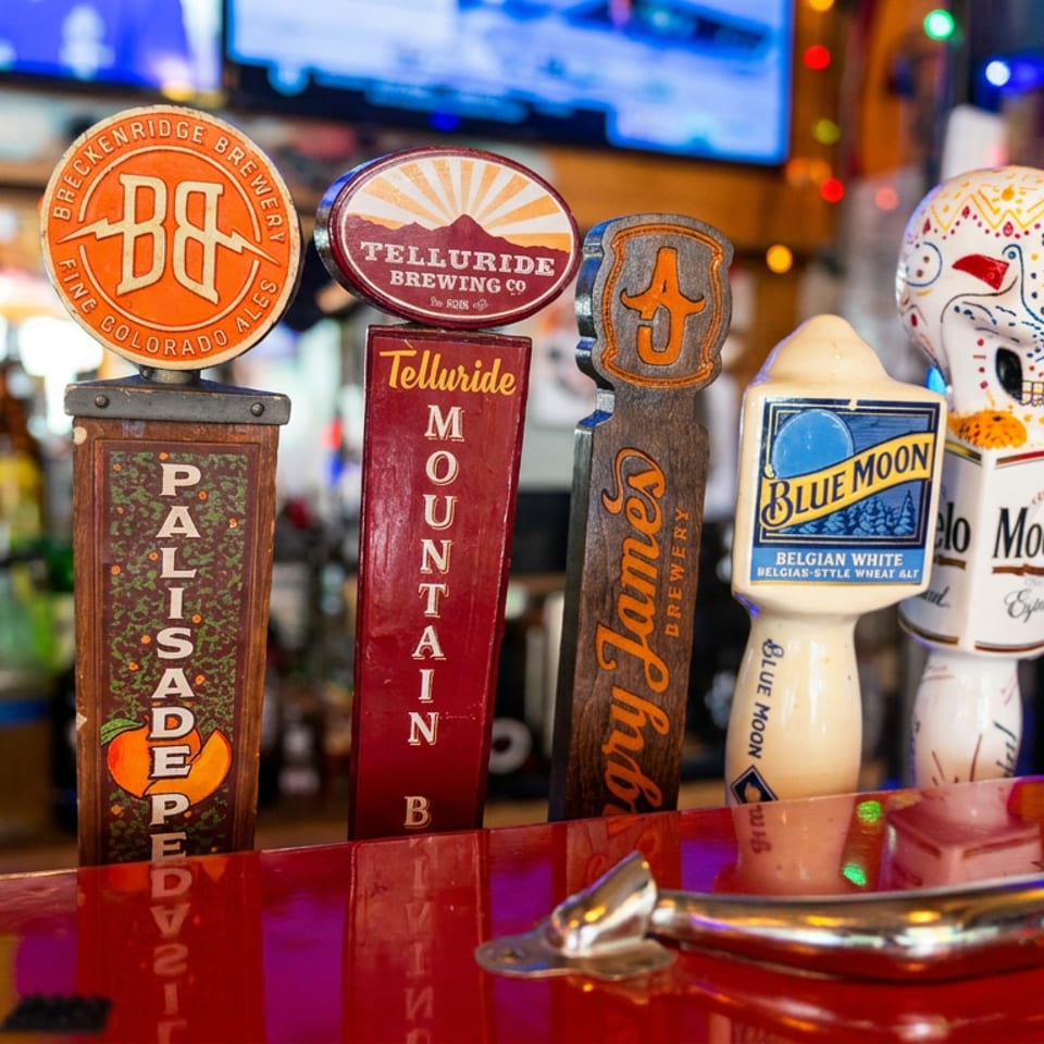 Colorful beer tap handles, including Colorado Rockies, Breckenridge Brewery, Telluride Brewing, Blue Moon, and Miller Lite, line a lively bar.